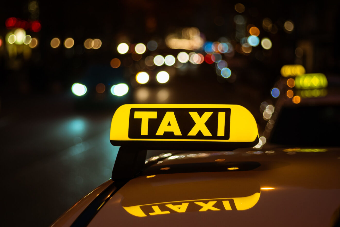 segno giallo e nero di taxi posto sopra un auto di notte